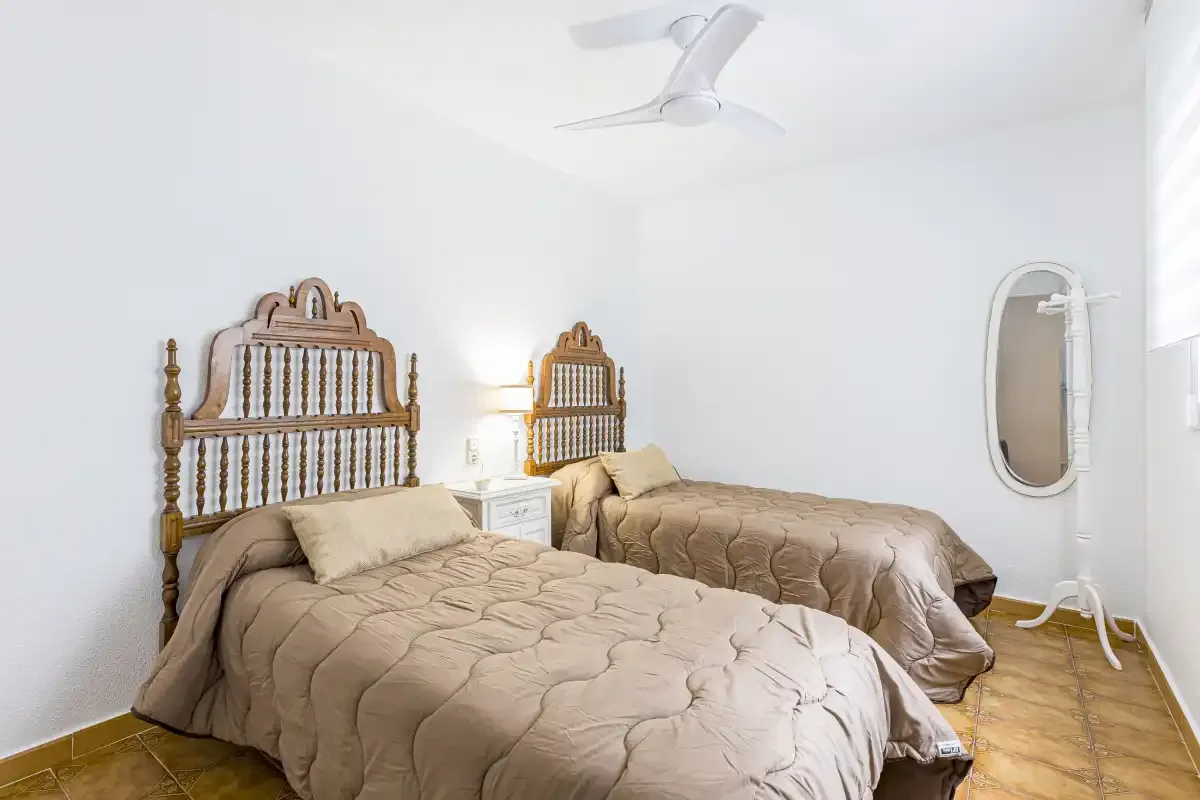 A bedroom with two beds, bedside tables, and a ceiling fan.