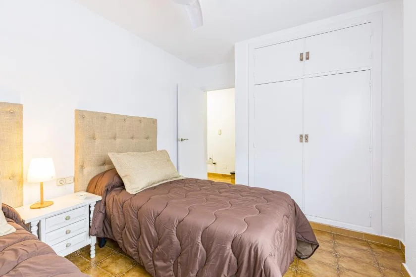 A bright bedroom with a bed, bedside table, and built-in white closet.