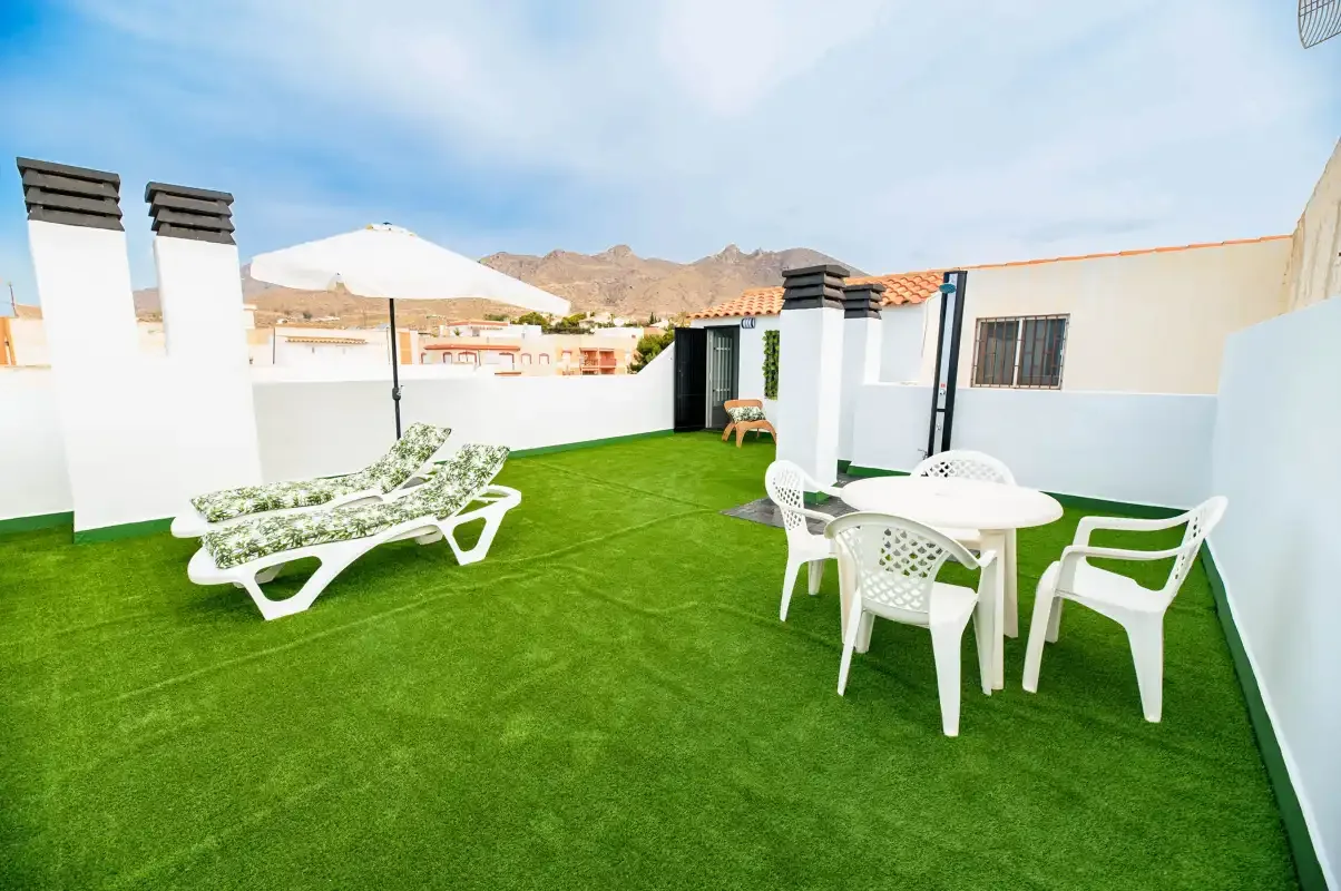 A rooftop terrace with green artificial turf, lounge seating, and a patio table.