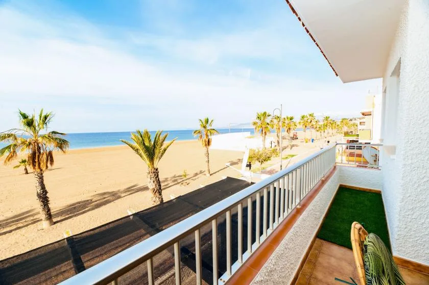 A balcony overlooks a sandy beach, palm trees, and the sea.