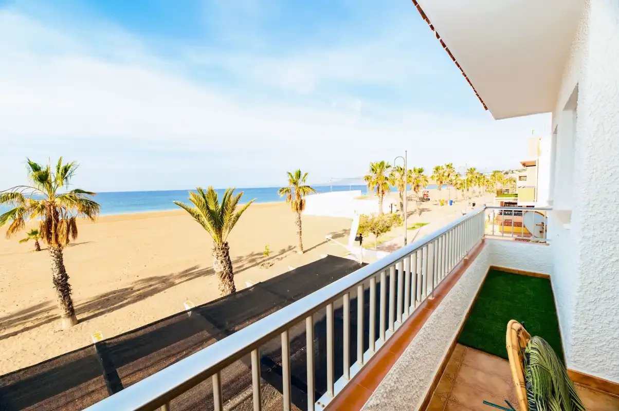 A balcony overlooks a sandy beach lined with palm trees.
