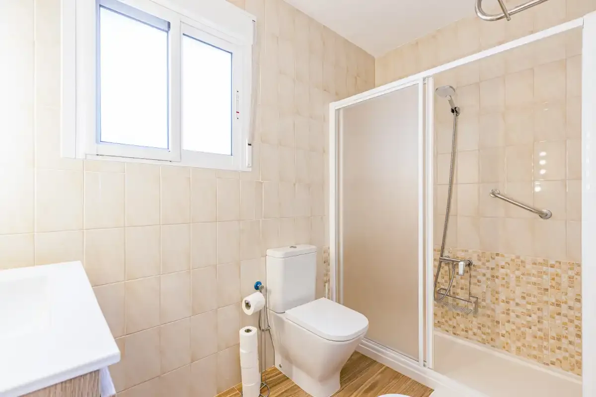A tiled bathroom with a toilet and glass-enclosed shower.