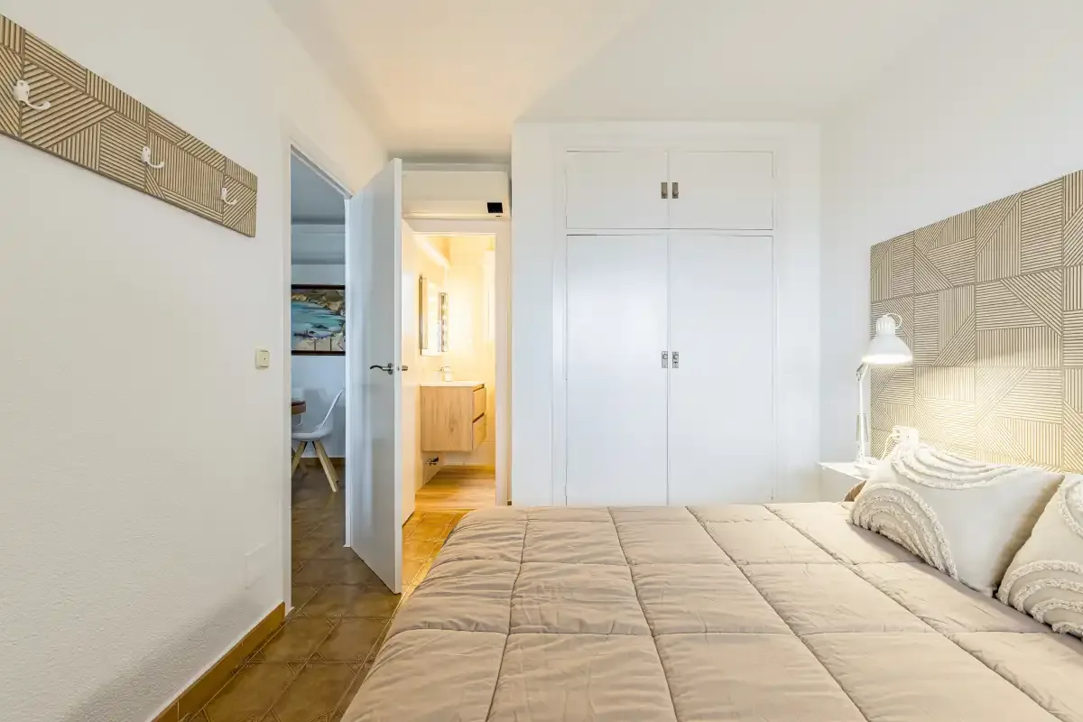 Bedroom with a bed, built-in wardrobes, and an open doorway to a lit hallway.