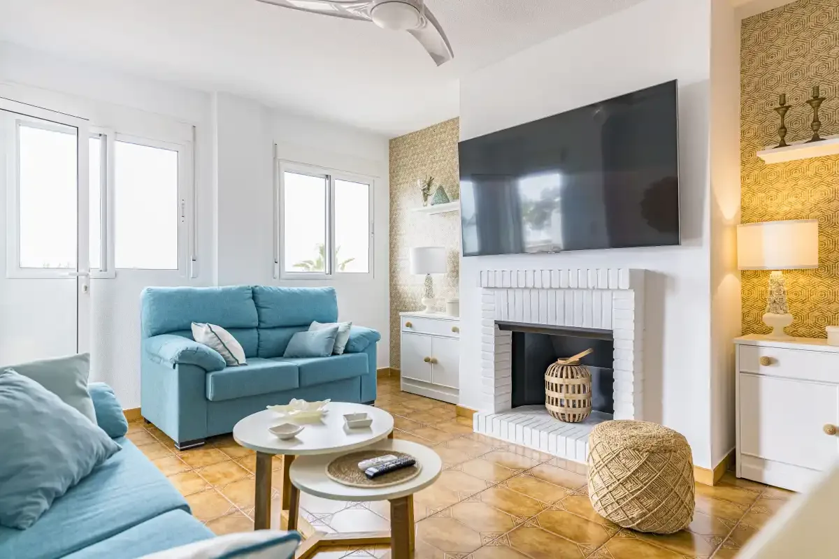 A bright living room with blue seating, a fireplace, and a wall-mounted television.