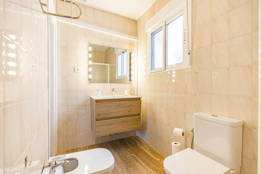 A tiled bathroom with a vanity, mirror, window, and toilet.