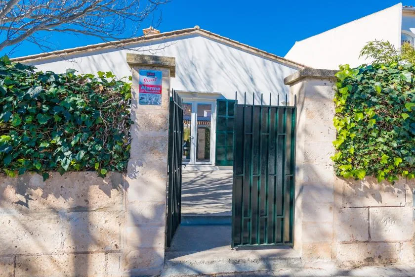 A gated entrance in a low white building, framed by leafy hedges.