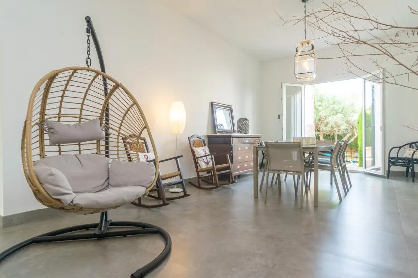 A bright dining and sitting area with a hanging chair and glass doors opening outside.