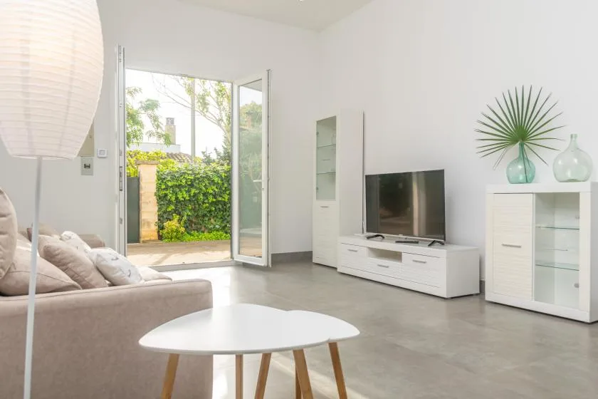 Bright living room with a television, low seating, and an open glass door to greenery.