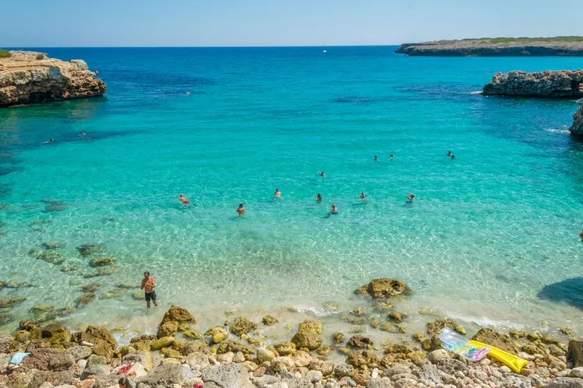 A turquoise bay with swimmers in clear water and a rocky shoreline.