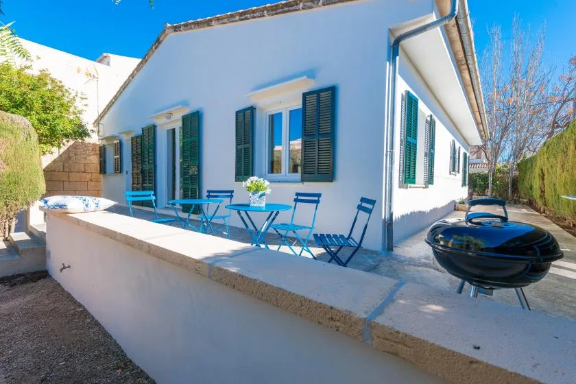 A sunny outdoor patio beside a white building, with blue seating and a grill.