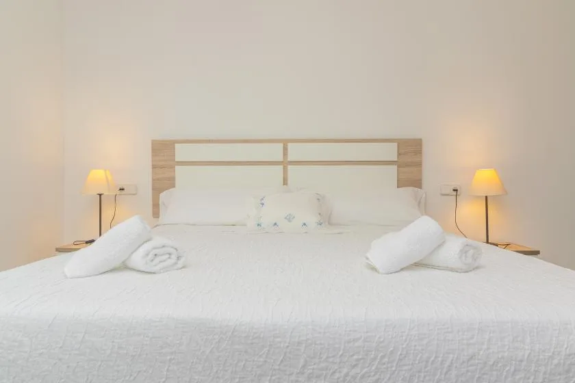 A neatly made bed with white linens and bedside lamps.