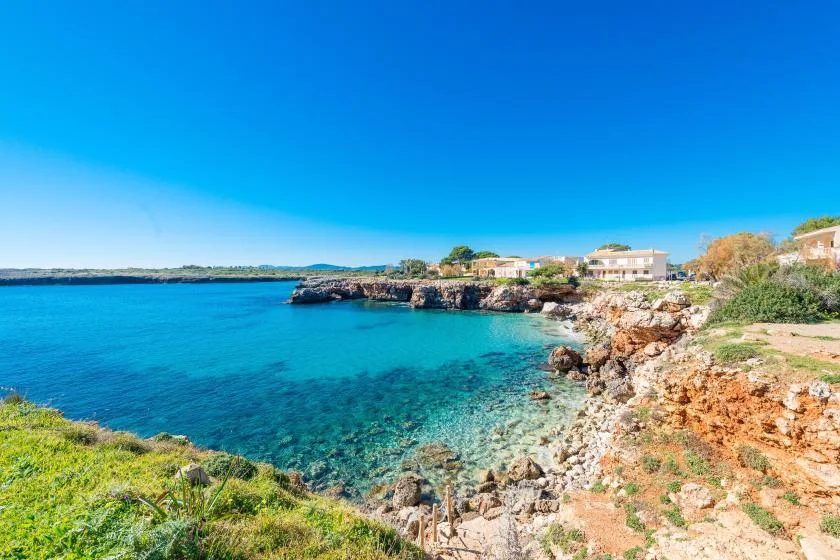 A clear turquoise bay meets a rocky shoreline beneath a bright blue sky.