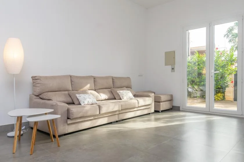 A bright living room with beige seating beside glass doors opening onto greenery.