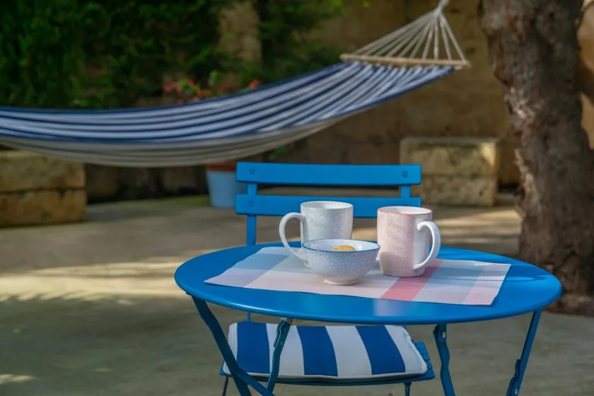 A blue outdoor table with cups sits beneath a striped hammock.