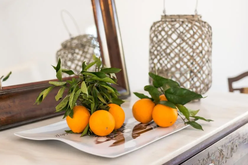 A tabletop display with oranges and leafy branches beside a framed mirror.