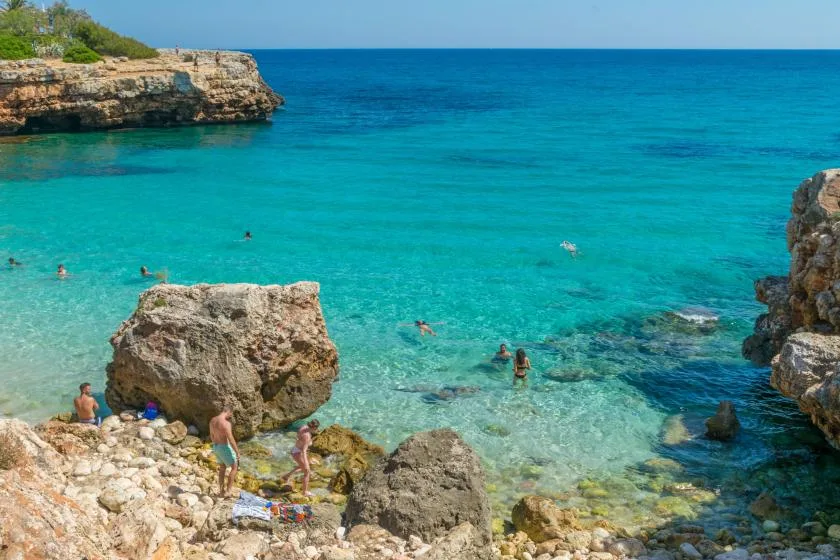 A clear turquoise sea meets a rocky shoreline where people are swimming.