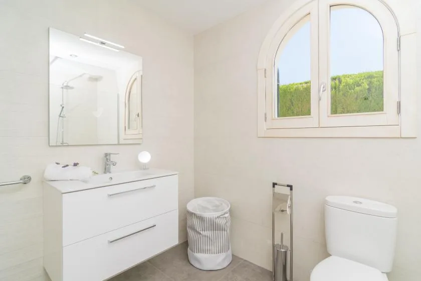 A bright bathroom with a vanity, mirror, and arched window.