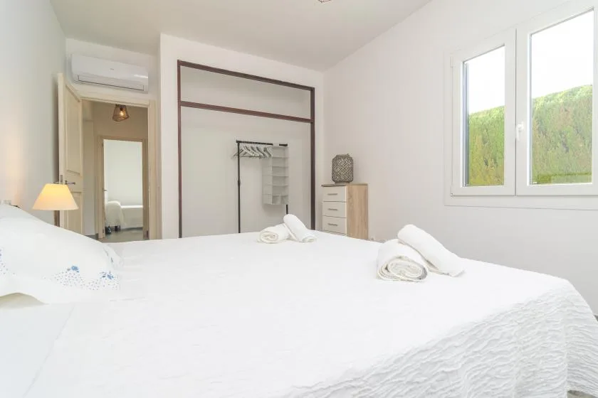 A bright bedroom with a neatly made bed and a window overlooking greenery.