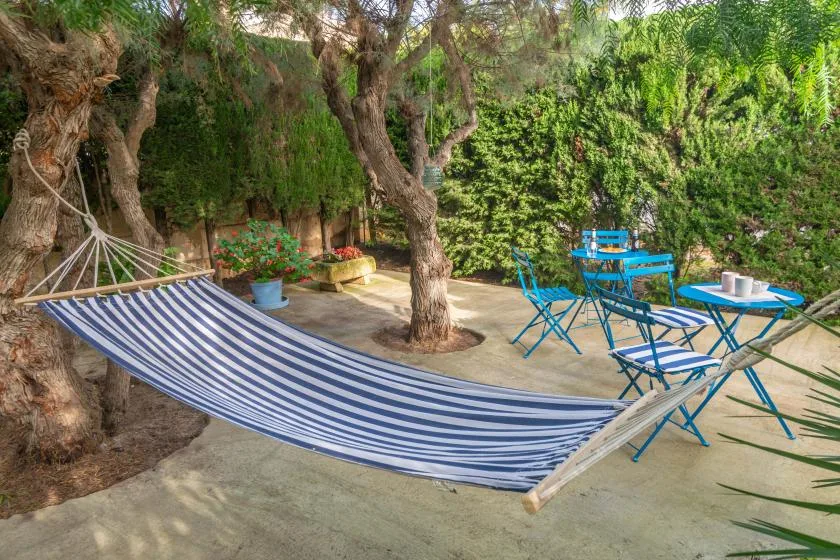 A shaded garden patio features a striped hammock and blue outdoor seating.
