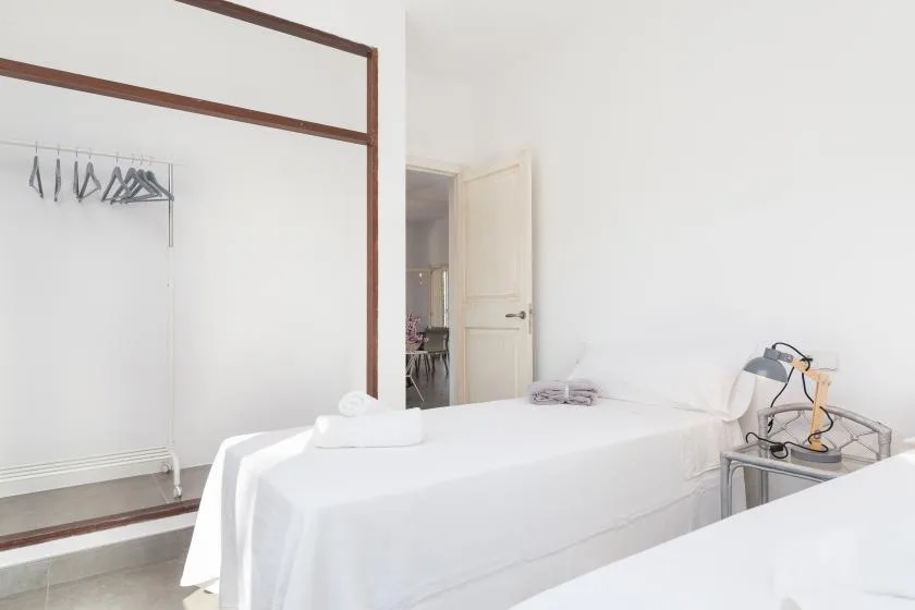 A bedroom with white bedding and an open clothing area beside the bed.