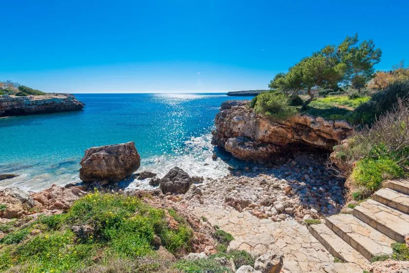 A rocky seaside cove with clear blue water and stone steps along the shore.