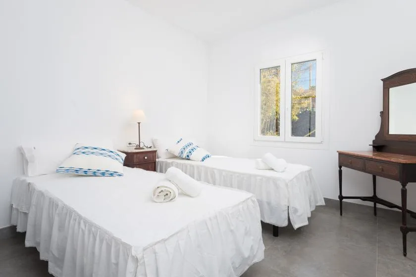 A bright bedroom with two beds and a window overlooking trees.