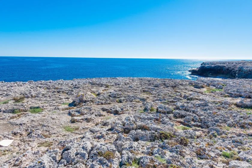 A rocky coastal landscape stretches toward the blue sea beneath a clear sky.