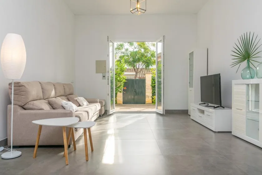 A bright living room with seating, a television, and open doors to a garden.