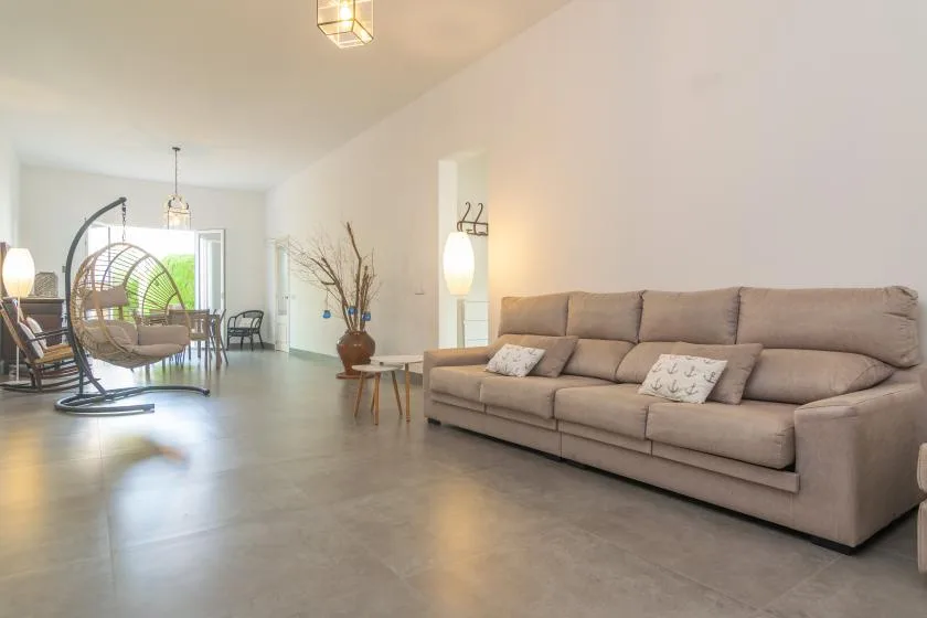A bright living room with a long sofa and a hanging chair near the window.