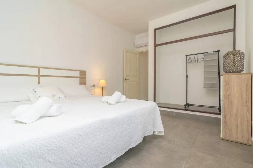 A bedroom with a large bed and a clothing rack in the background.