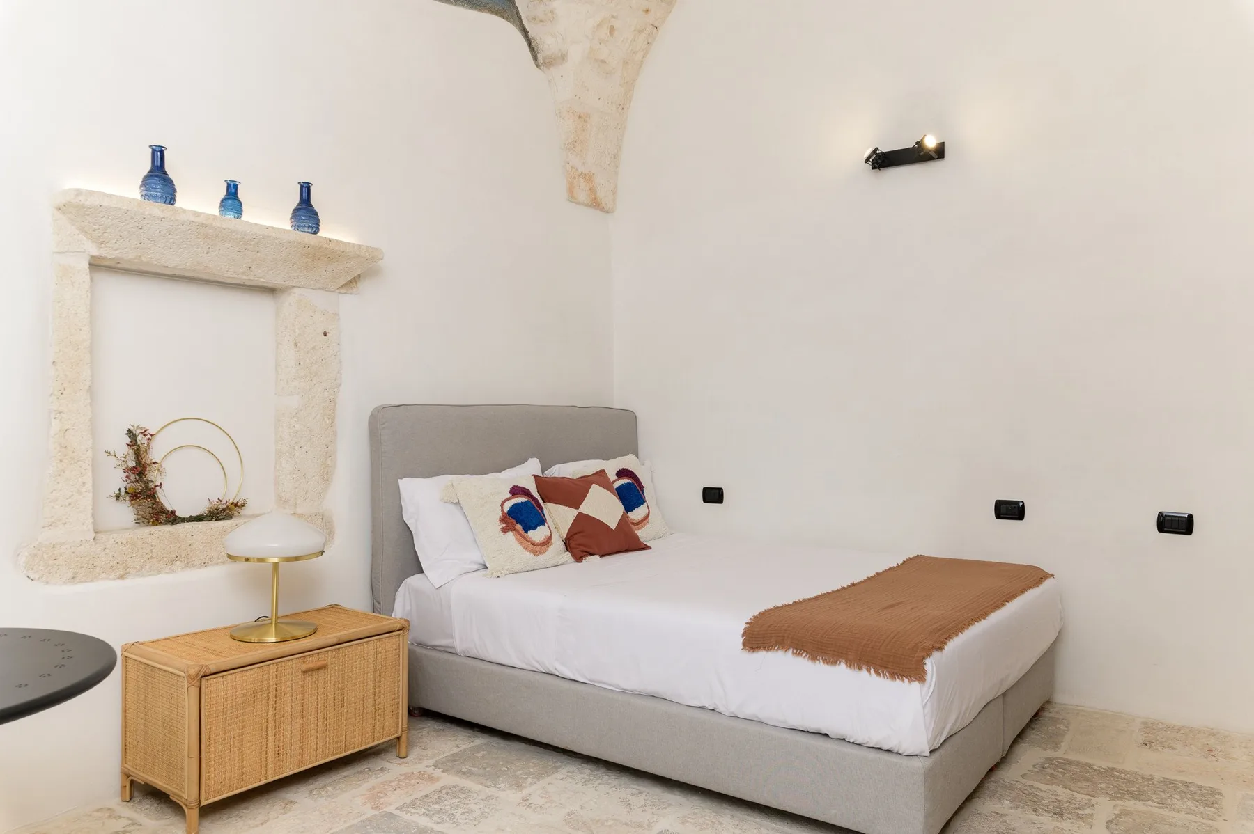 Un dormitorio con una cama, cojines decorativos y una pequeña mesa de noche.