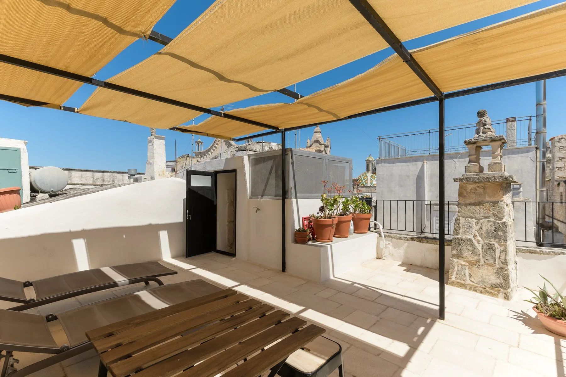 Una terraza soleada en la azotea con toldo, asientos al aire libre y plantas en macetas.