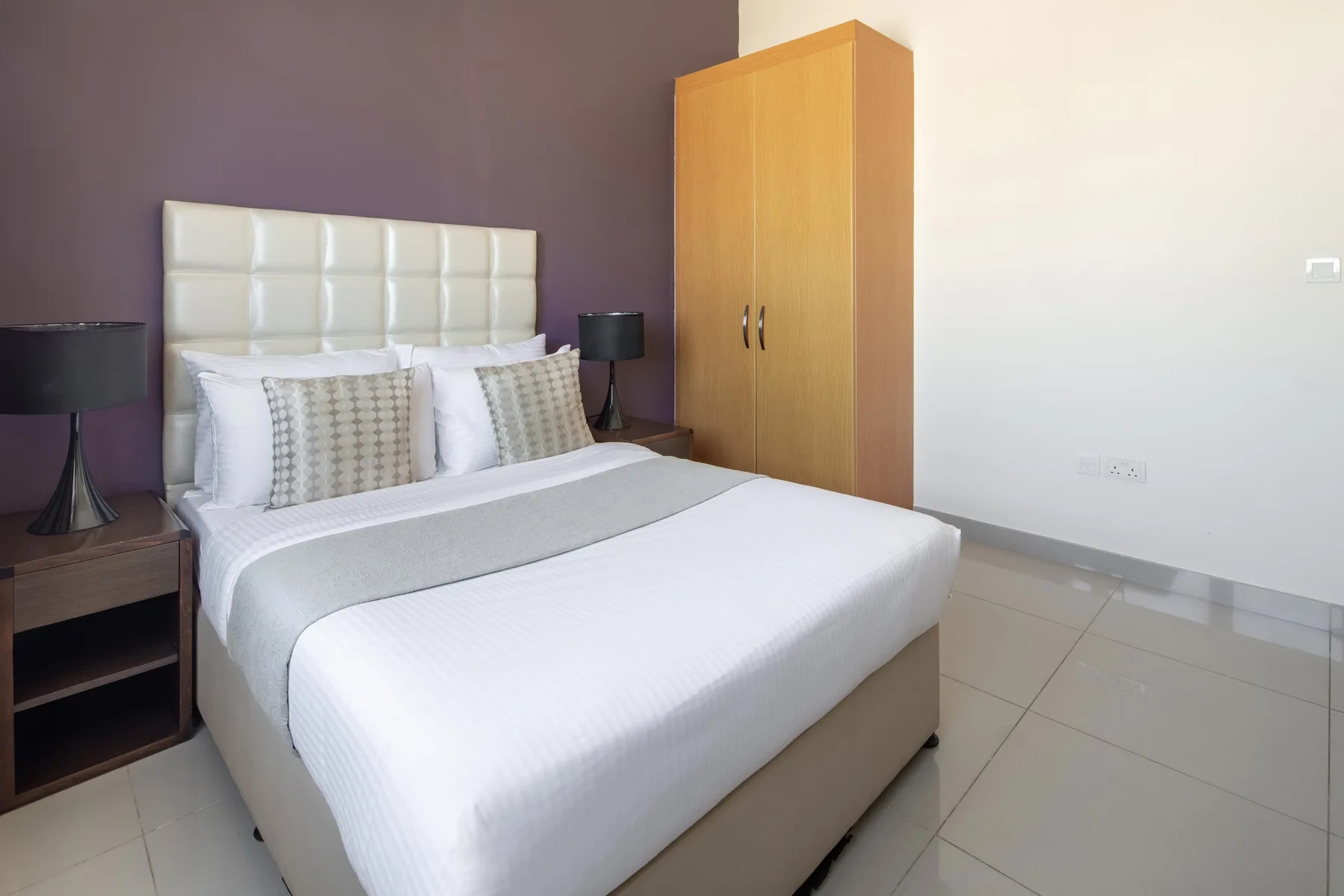 A bedroom with a neatly made bed, bedside tables, and a wardrobe.