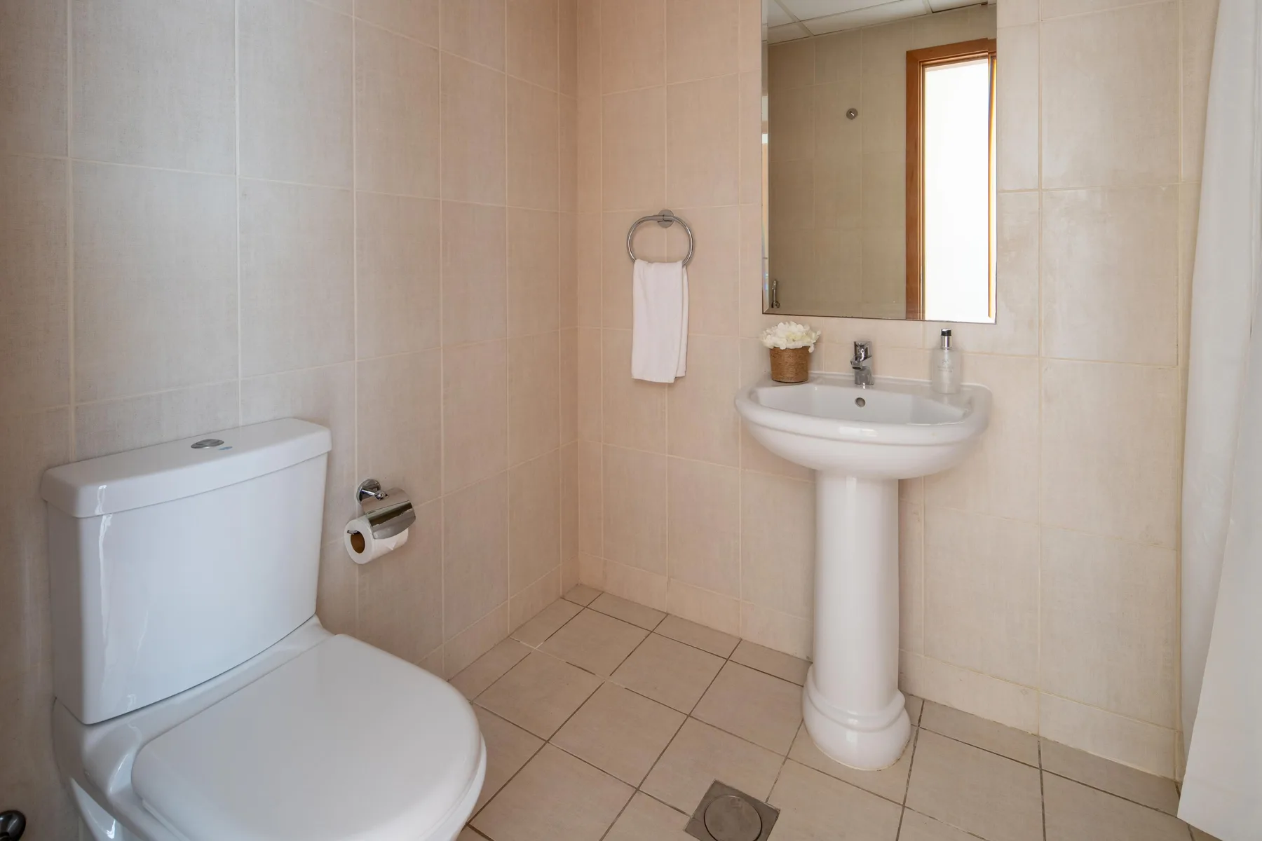 A tiled bathroom with a toilet, pedestal sink, and wall mirror.