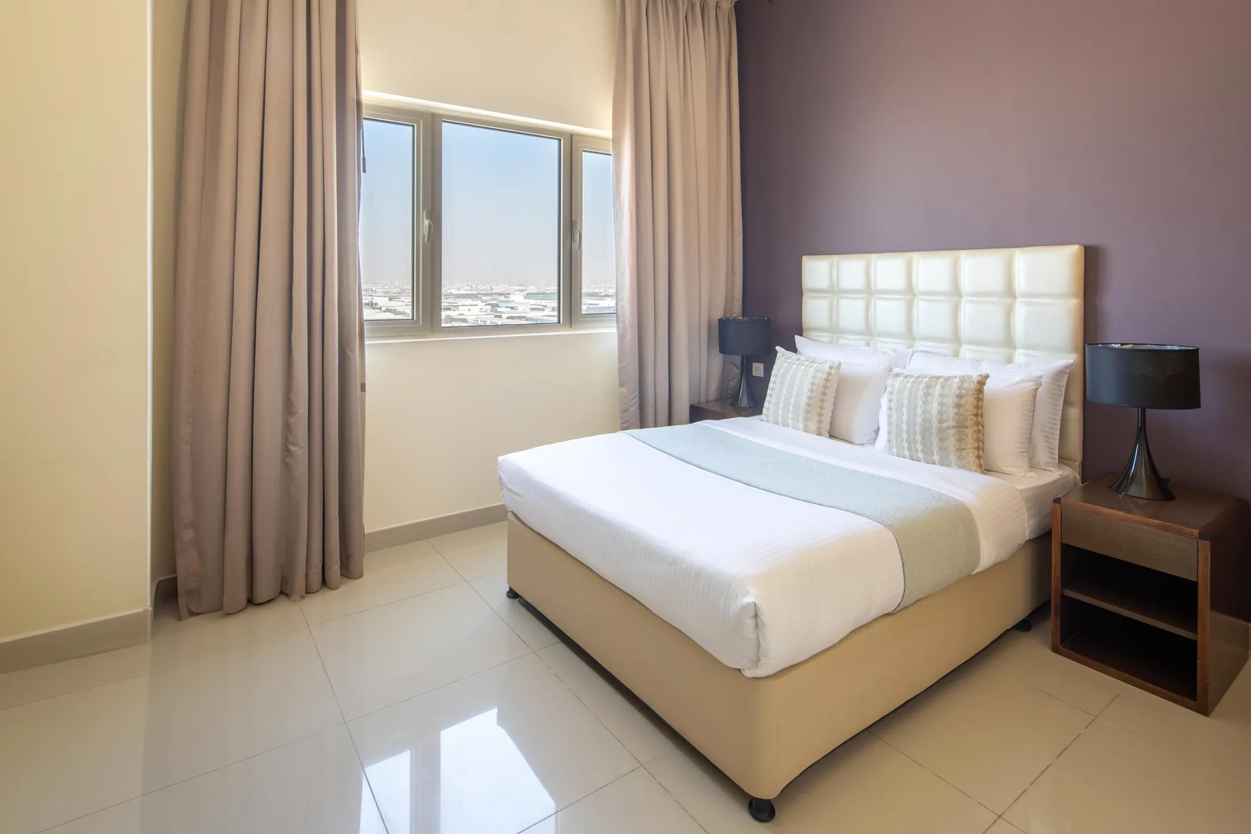 A bedroom with a bed beside a window framed by curtains.