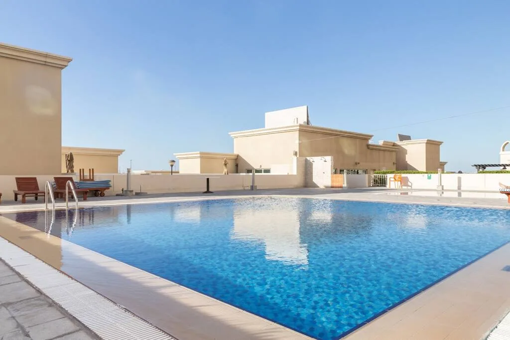A rooftop swimming pool reflects the blue sky beside low beige buildings.