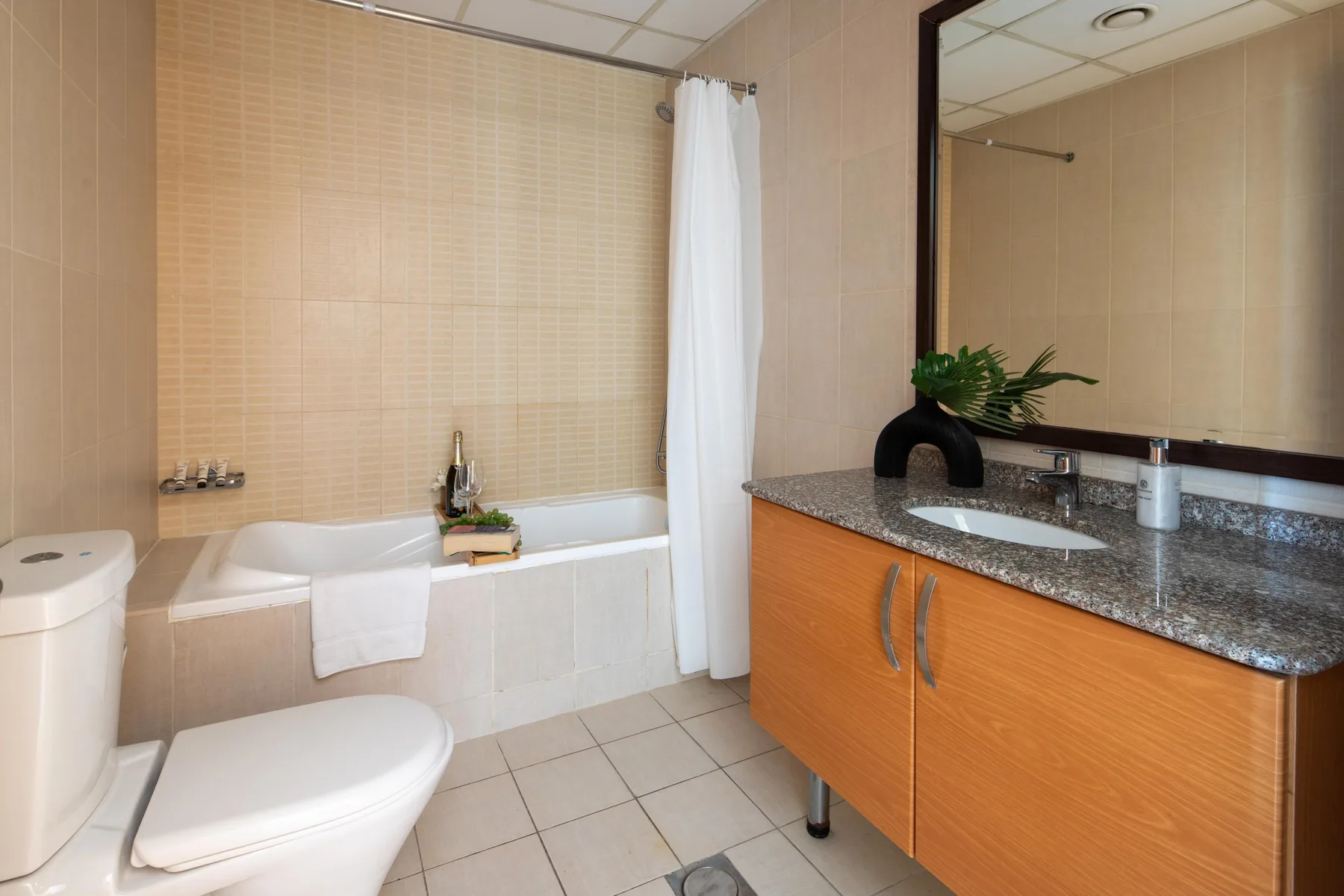 A tiled bathroom with a bathtub, shower curtain, toilet, and vanity.