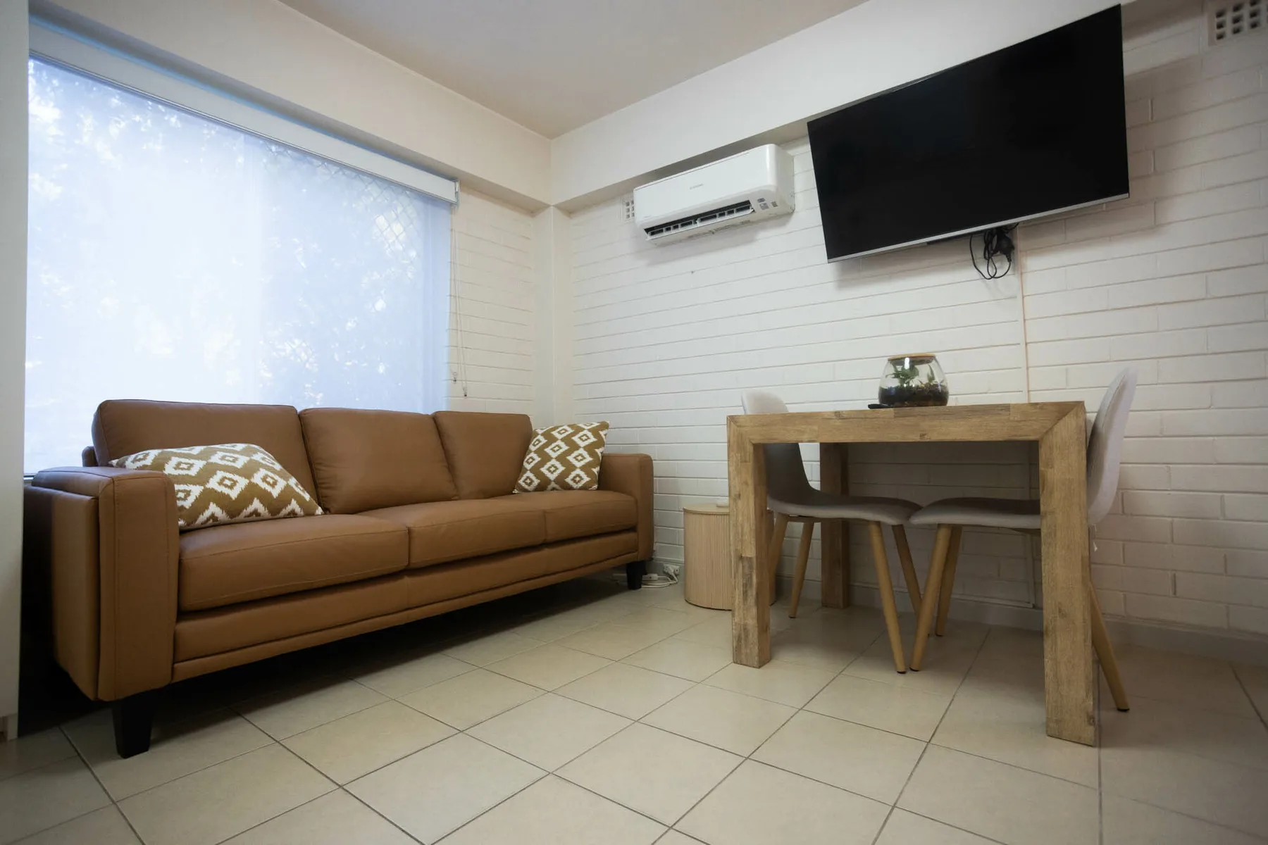 Una sala amueblada con un sofá marrón, una mesa de madera y un televisor en la pared.