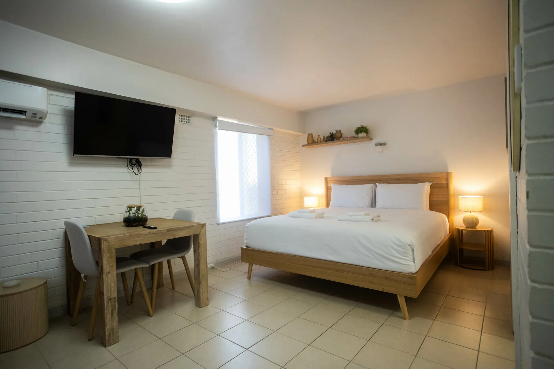 Un dormitorio con una cama doble, escritorio, televisor y suelo de baldosas.