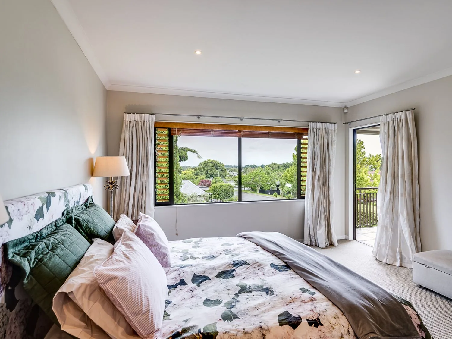 A bedroom with a bed and a wide window overlooking greenery.