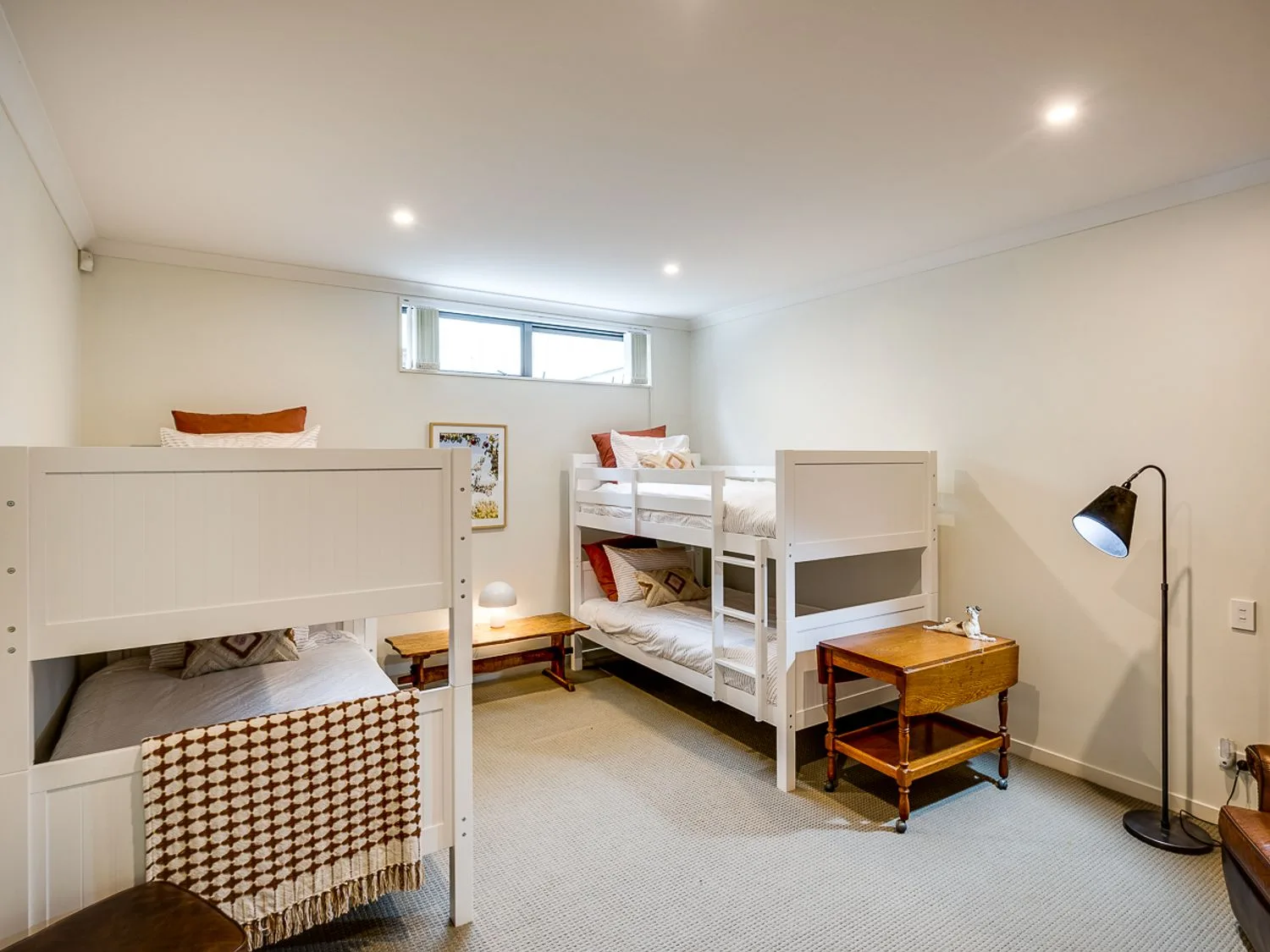 A bedroom with two white bunk beds a wooden bedside table a floor lamp and a small window at Busby Hill Villa - Havelock North Holiday Home in Havelock North