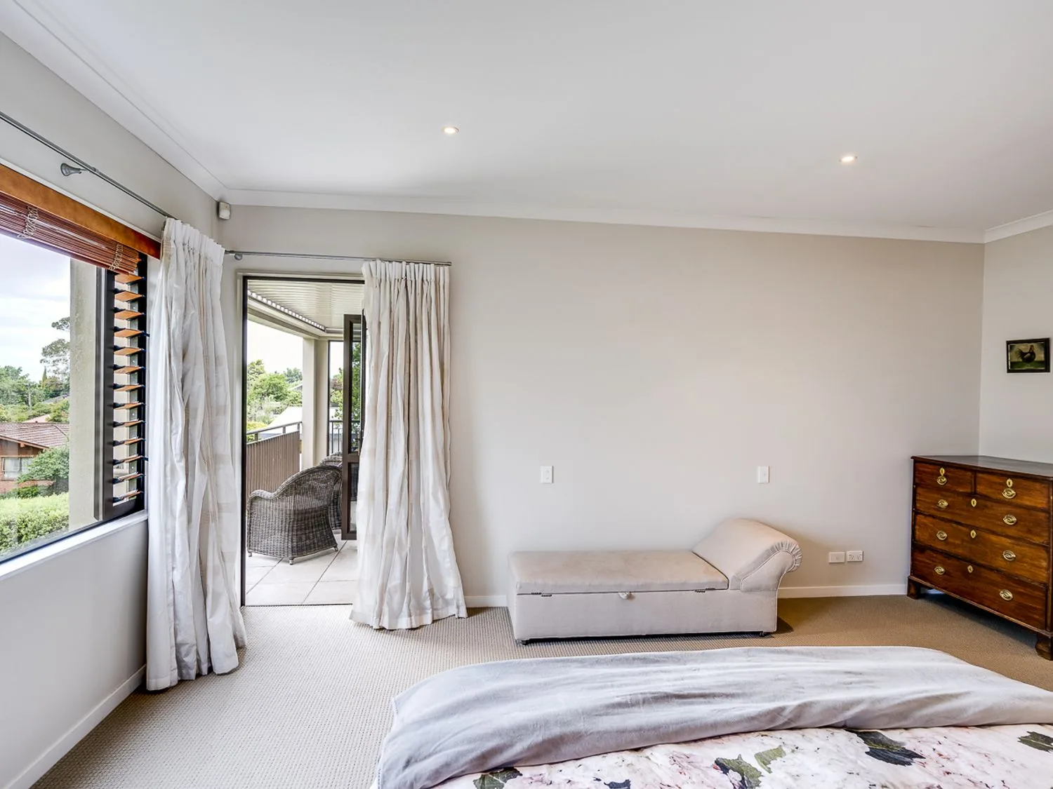 A bedroom with a bed, a chaise lounge, and a curtained doorway opening onto a balcony.