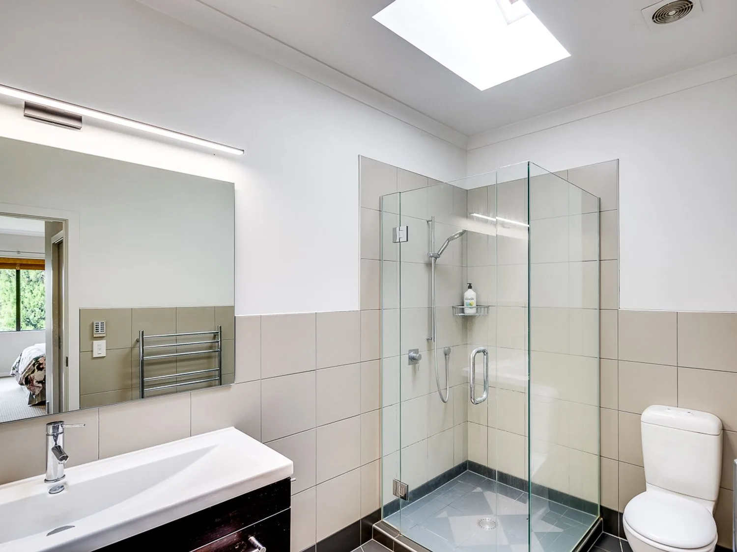 A bright bathroom with a sink, mirror, toilet, and glass shower.