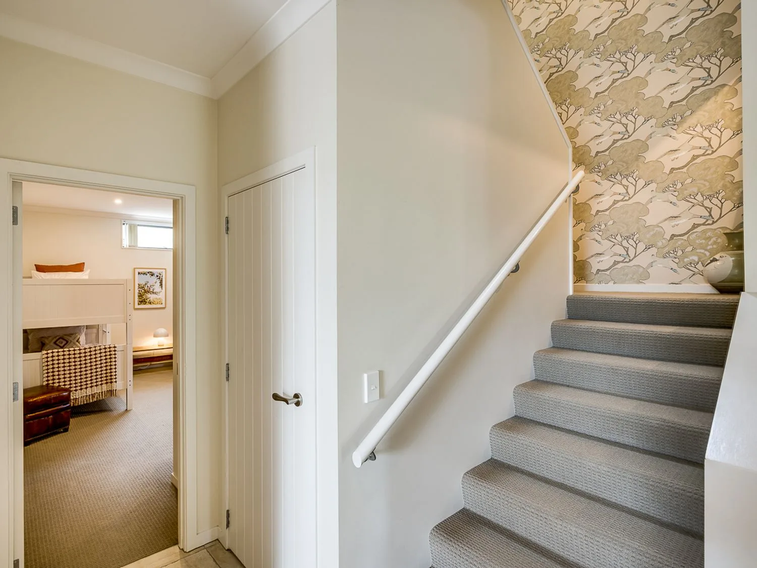 A carpeted staircase with a handrail beside an open doorway to a bedroom.