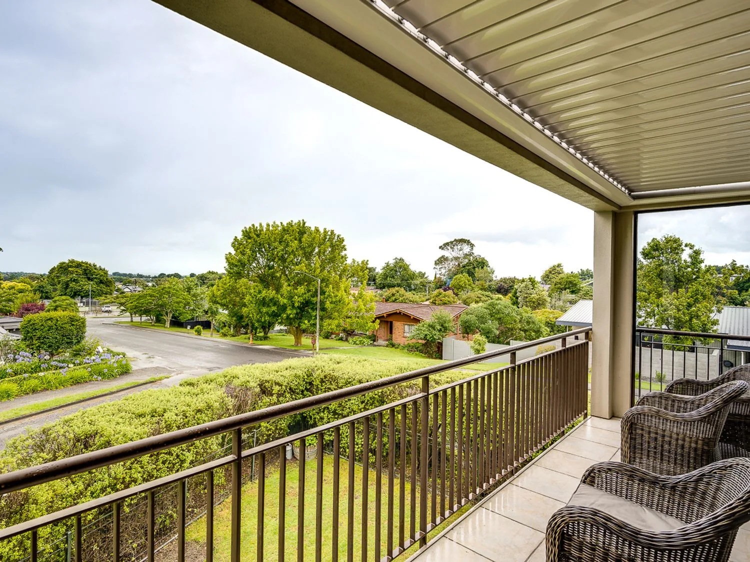 A balcony with wicker chairs overlooking a street and trees at Busby Hill Villa - Havelock North Holiday Home in Havelock North
