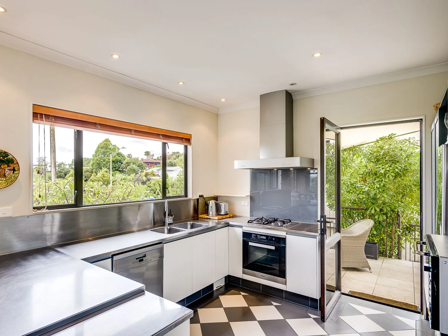 A modern kitchen with a cooking range and an open door to a leafy patio.