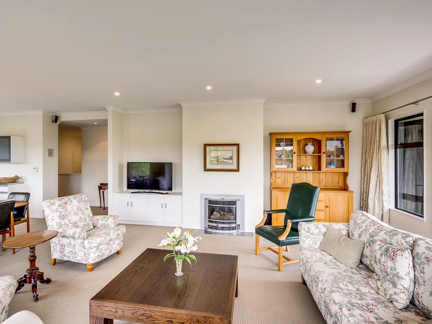 A living room with floral seating, a dark coffee table, a television, and a fireplace.