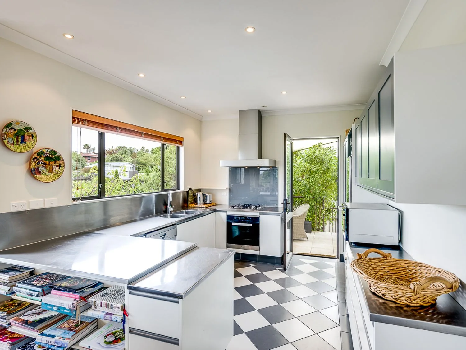 A bright kitchen with stainless steel counters, a large window, and a black-and-white tiled floor.