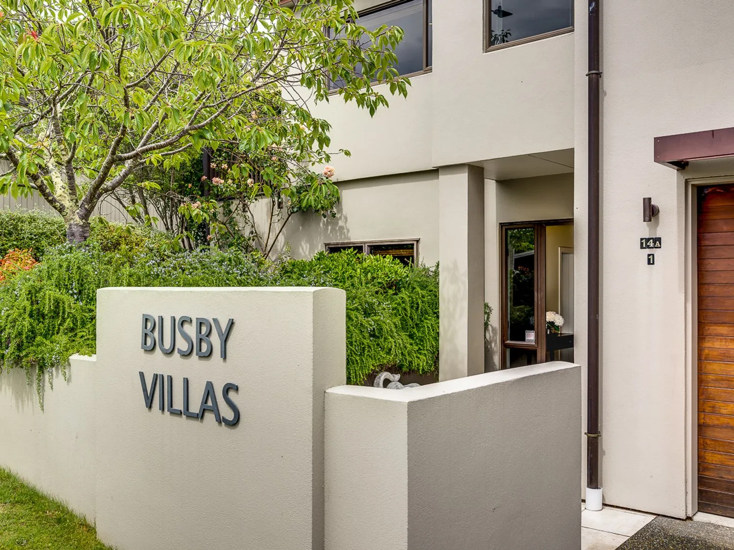 The exterior entrance of a villa features a Busby Villas sign and surrounding greenery.