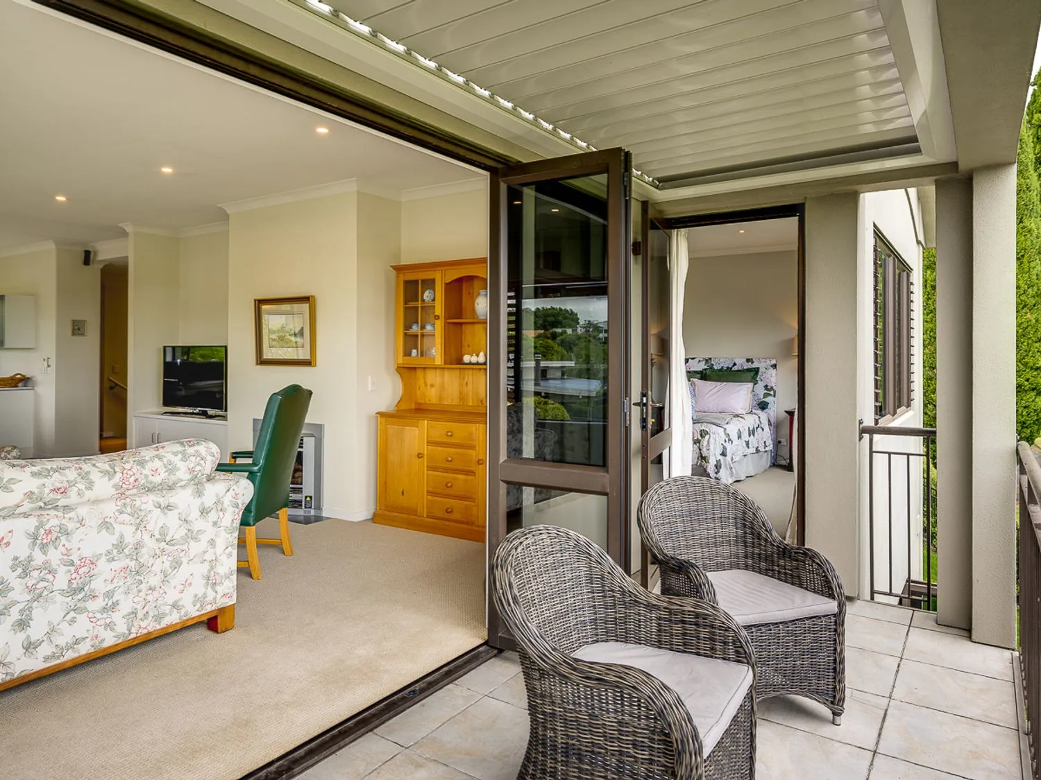 A covered balcony with wicker seating opens onto a living area and bedroom.